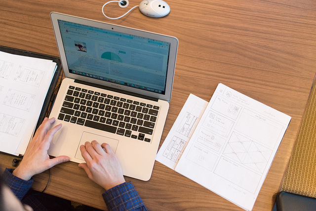 Laptop computer sitting on a desk with hands typing on it